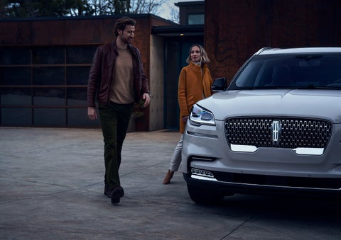 A man and a woman approaching a 2024 Lincoln Aviator® SUV, which illuminates certain lights when they are close | Sheehy Lincoln of Richmond in Richmond VA